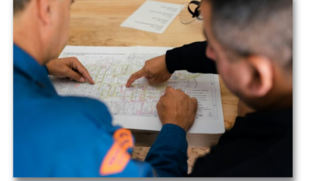 Two people study a large map on a wooden table, one pointing to a detail as they discuss collaboratively.